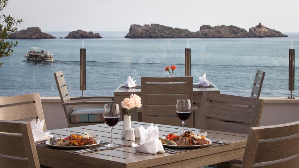 Eleganta restorāna terase ar skatu uz jūru un salām, uz galda pasniegti gardi ēdieni un sarkanvīns. Ideāla vieta romantiskai vai relaksējošai maltītei.