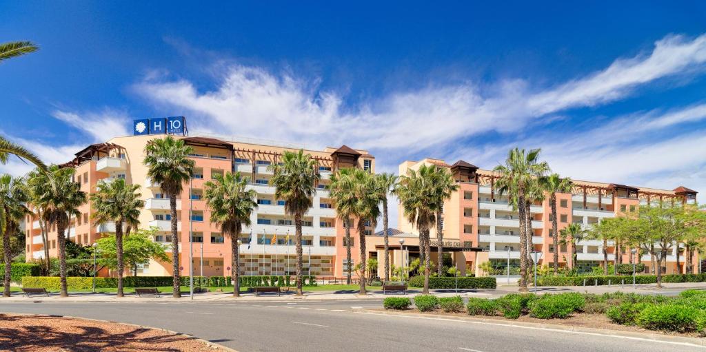 Moderns viesnīcas ēkas attēls ar palmu rindām un skaidru zilu debesi fonā. Viesnīca ir H10 zīmola, piedāvājot pievilcīgu arhitektūru un labiekārtotu apkārtni.
