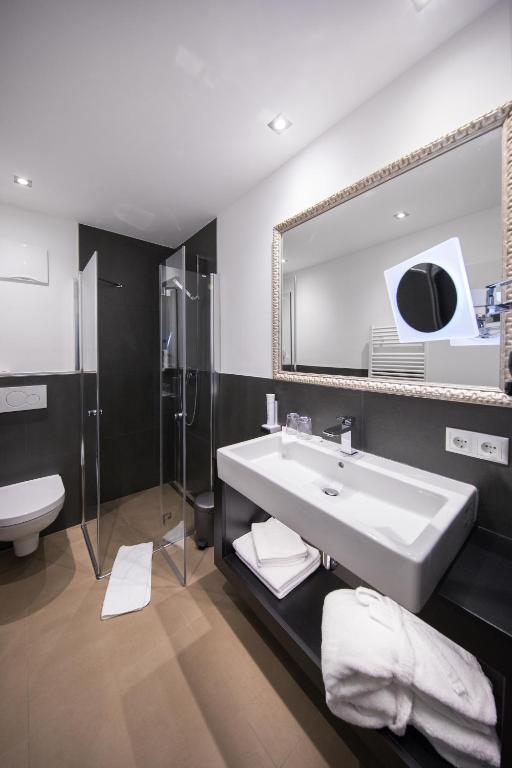 Mūsdienīgs vannas istabas interjers ar stikla dušu, elegantu izlietni un spoguli. Telpa izceļas ar minimālistisku dizainu un neitrālām krāsām.