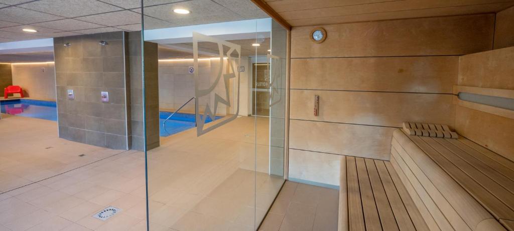 Mūsdienīga saunas telpa ar stikla sienu, kas nodrošina skatu uz peldbaseinu. Interjers ir gaišs un elegants, ar koka soli un modernām apgaismojuma iespējām.