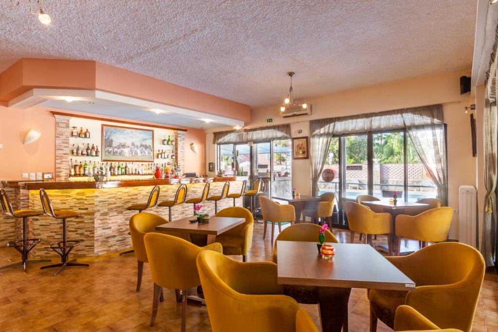 Mūsdienīgs bārs ar ērtām dzeltenām krēslām un elegantu koka galdu, kurā ir plašs dzērienu klāsts, gaiša apgaismojuma un lieliem logiem, kas piedāvā skatu uz ārpusi.