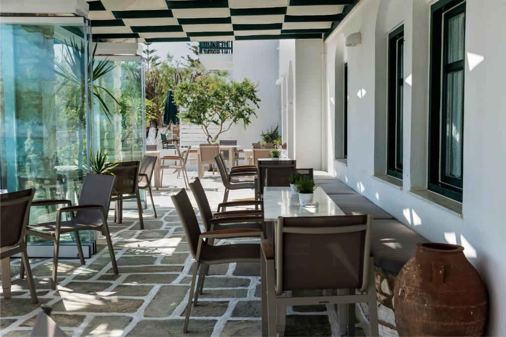 Mūsdienīgs restorāna terases interjers ar stikla sienām un zaļām augiem, kurā ir galds un krēsli, nodrošinot patīkamu atpūtu saulainā dienā.