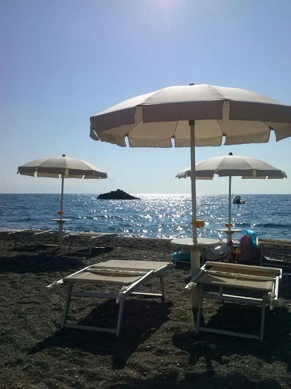 Pludmales ainava ar saulessargiem un atpūtas krēsliem, skaidra jūra un saule, kas atspoguļojas uz ūdens virsmas.