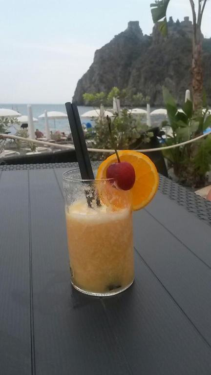 Vasaras kokteilis ar apelsīnu šķēli un ķiršu dekoru, fons ar pludmali un kalnu ainavu.