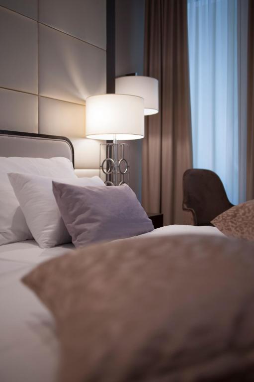 Mūsdienīgs guļamistabas interjers ar ērtām spilvenām un gaismas avotiem, radot relaksējošu atmosfēru. Dabiska gaisma plūst caur logu, piešķirot telpai siltumu.