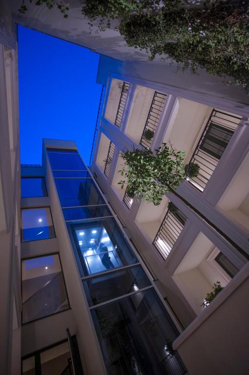 Mūsdienīga ēka ar stikla elementiem un balkoniem, redzama no apakšas uz zilu debesu fonu. Gaismas avots izgaismo iekšējo telpu.