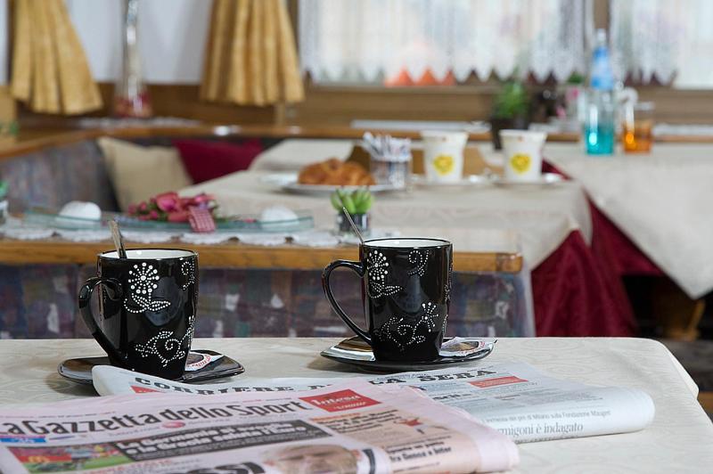 Divas melnas krūzes ar rotājumiem uz galda, blakus avīzei, kas atrodas kafejnīcā ar mājīgu interjeru.