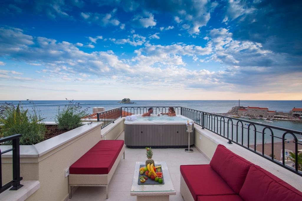 Terases skats uz jūru ar burbuļvannu un sarkaniem dīvāniem, kas nodrošina relaksējošu atmosfēru. Svaigi augļi uz galda papildina ainavu ar mājīgu noskaņu.