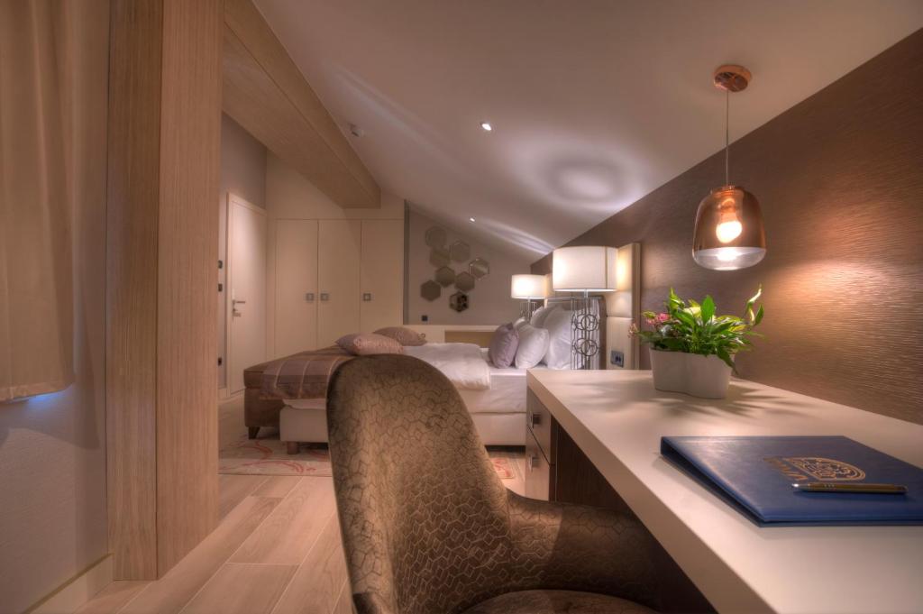 Mūsdienīgs guļamistabas interjers ar darba galdu, ērtu krēslu un dekoratīviem gaismas avotiem. Telpa ir gaiša un eleganta, radot patīkamu atmosfēru.