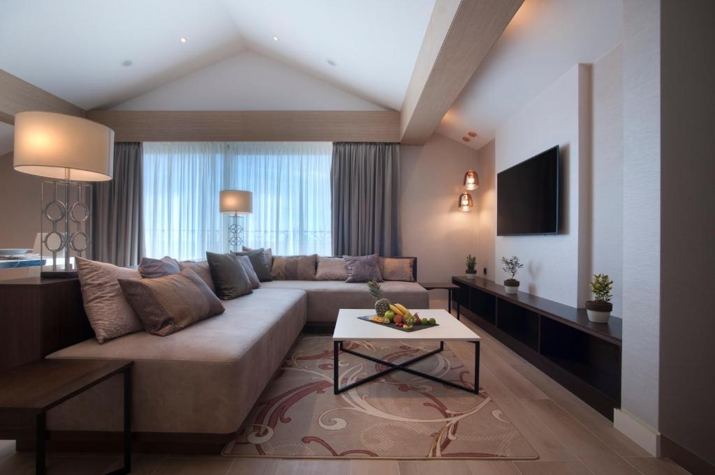 Mūsdienīga viesistaba ar ērtu dīvānu, stilīgām lampām un TV, papildināta ar dekoratīvām augu kompozīcijām. Gaismas plūstošais interjers rada mājīgu atmosfēru.