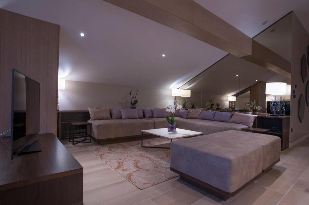 Mūsdienīgs viesistabas interjers ar ērtu dīvānu, elegantu gaismu un dekoratīvām augu kompozīcijām. Telpa ir gaiša un plaša, radot patīkamu atmosfēru.