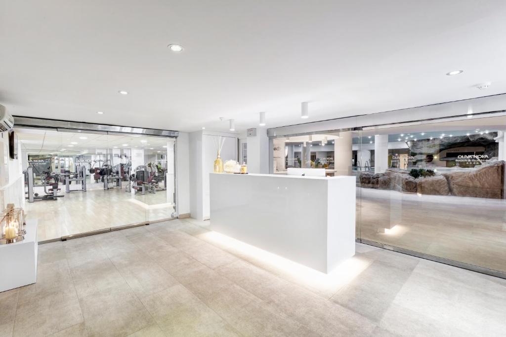 Mūsdienīgs sporta zāles reģistrācijas punkts ar stikla durvīm, kas ved uz treniņu zonu. Interjers ir gaišs un elegants, ar baltu reģistrācijas letni un modernu aprīkojumu.