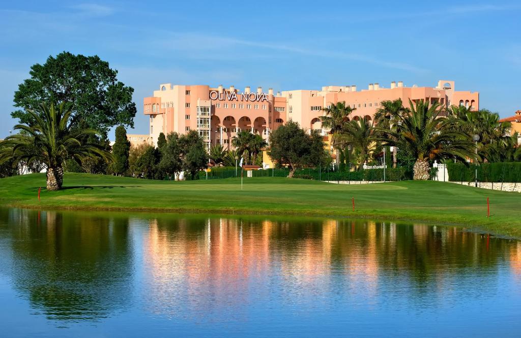 Oliva Nova golfa laukuma ainava ar palmām un ūdens atspulgu, fons ar viesnīcu.