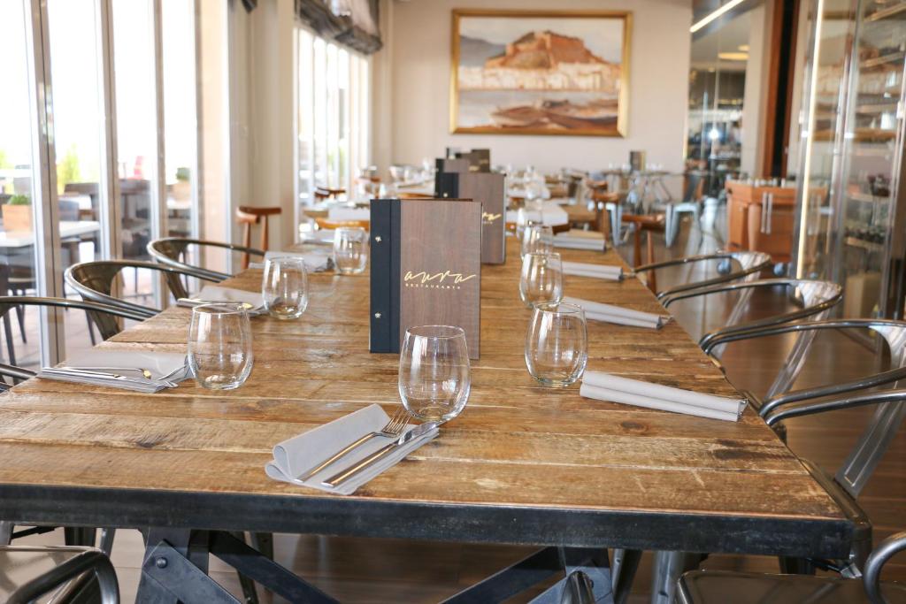 Mūsdienīgas restorāna iekārtojums ar koka galdu, glītām glāzēm un ēdienkarti. Gaisīga atmosfēra ar lieliem logiem, kas nodrošina dabu.