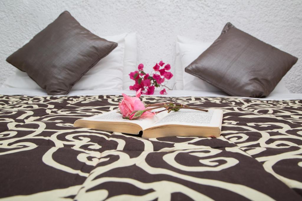 Gultā ar dekoratīviem spilveniem, atvērta grāmata un rozā ziedi, radot mierīgu un relaksējošu atmosfēru.