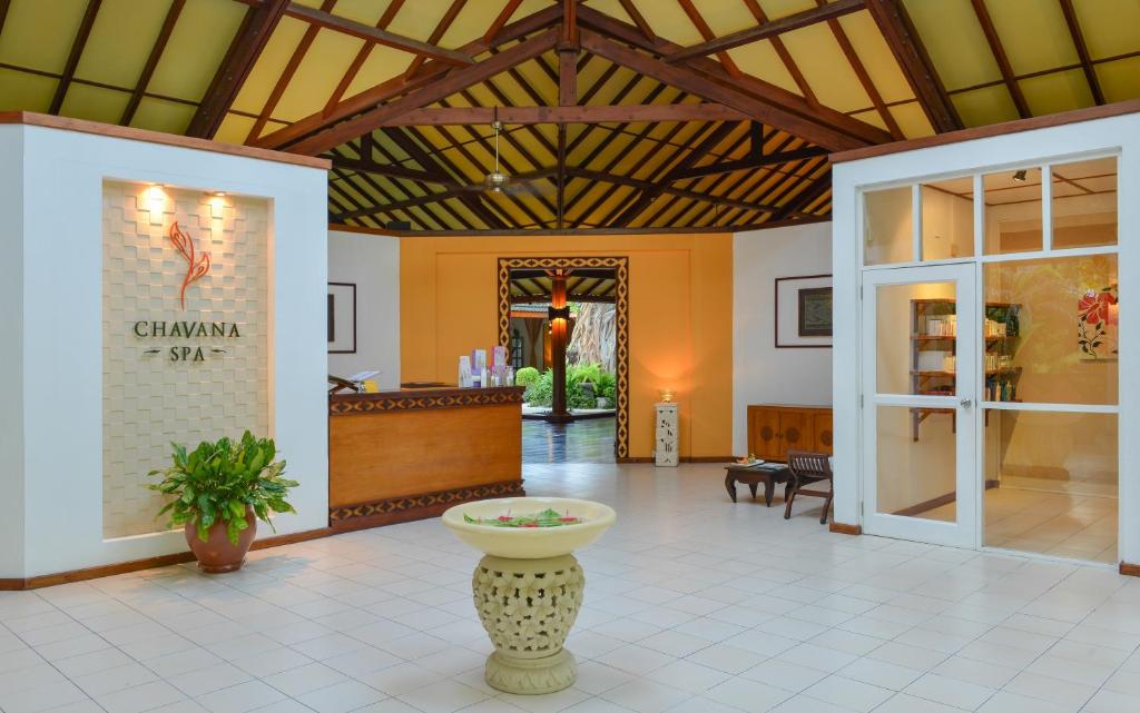 Elegants SPA interjers ar Chavana SPA logotipu, koka reģistratūru un zaļām augu kompozīcijām. Telpā ir gaiša apgaismojums un plašas telpas, kas rada relaksējošu atmosfēru.