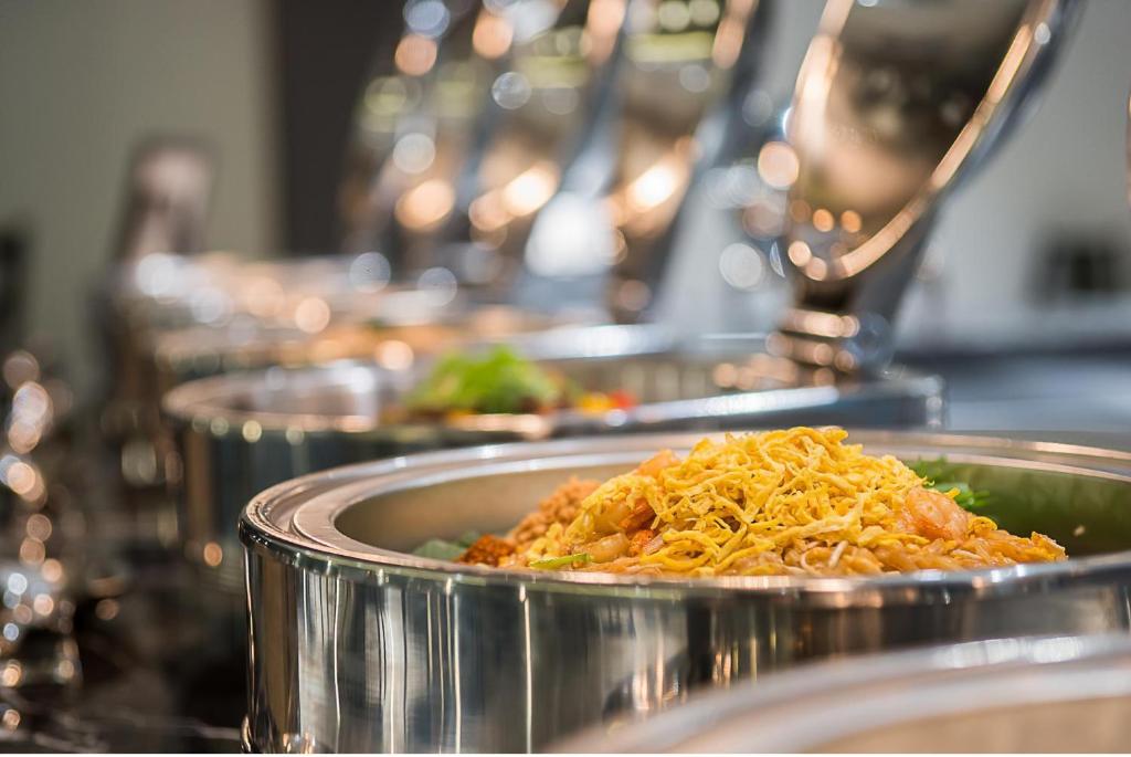 Svaigu ēdienu bufete ar dažādām delikatesēm, ieskaitot rīsus un dārzeņus, pasniegta spīdīgās traukos.