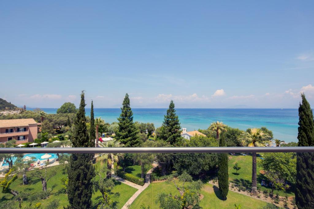 Skats uz jūru no balkona, kur redzami zili ūdeņi, krāšņi dārzi un zaļi koki. Ideāla vieta atpūtai un relaksācijai.