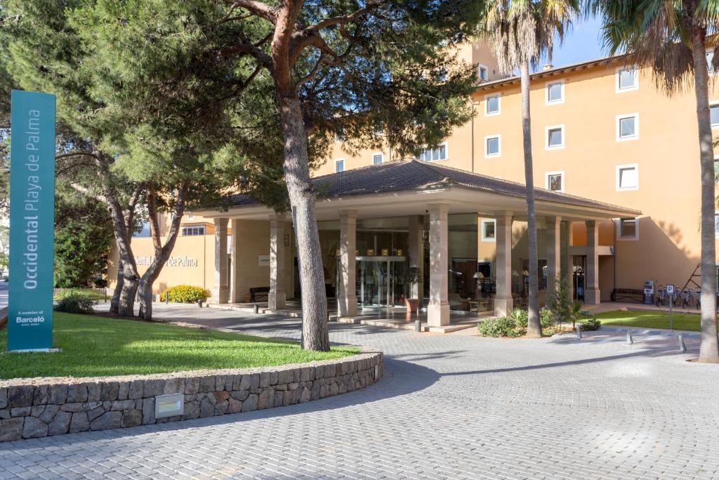 Viesnīcas Occidental Playa de Palma ieeja ar mūsdienīgu arhitektūru un zaļām ainavām. Apkārt viesnīcai ir koku alejas un labi kopta zālāja platība.