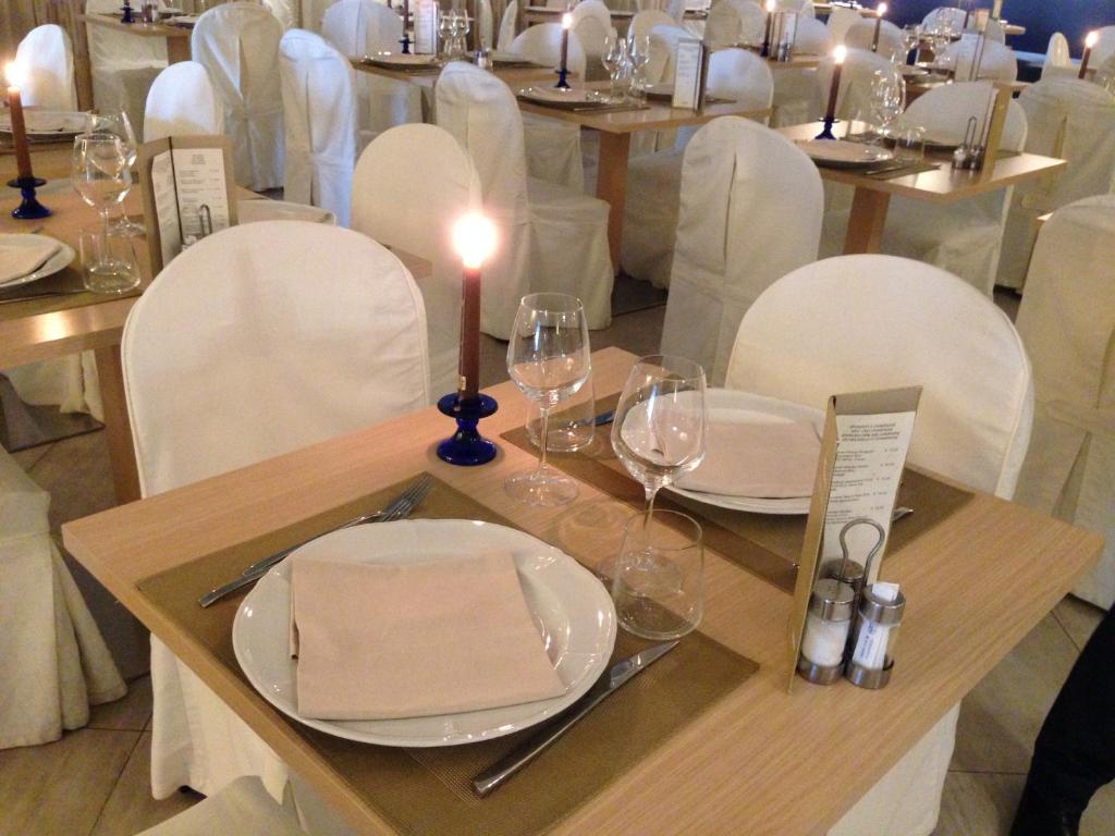 Eleganti izkārtots restorāna galds ar krēslām, sveci un galda piederumiem. Galds ir klāts ar baltu galdautu un dekorēts ar glāzēm un ēdienkarti.