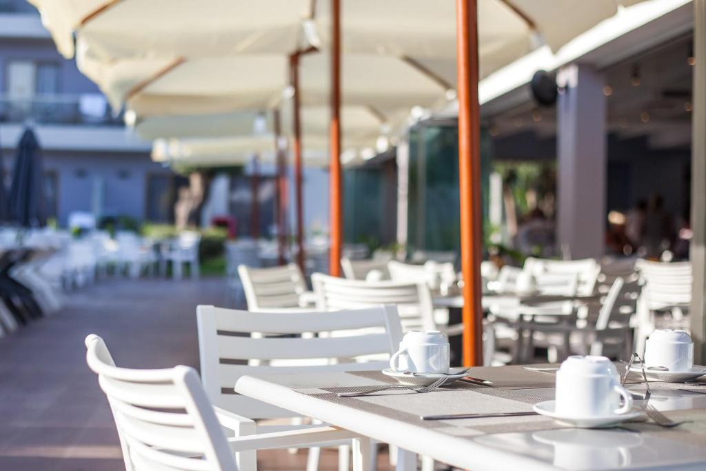 Āra kafejnīca Sunny Days Hotel-Apartments ar baltām mēbelēm un kafijas krūzēm.