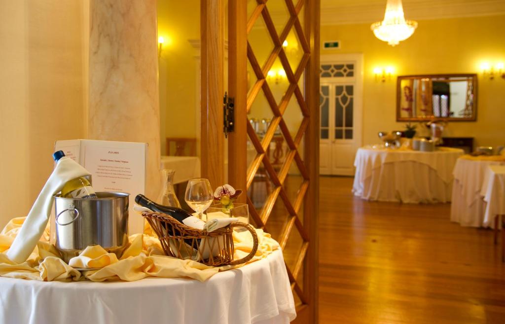 Elegants restorāna interjers ar galdu, uz kura atrodas vīna dzesētājs un glītas glāzes, radot svinīgu atmosfēru. Fons ir gaiši dzeltena telpa ar izsmalcinātiem apgaismojuma elementiem.