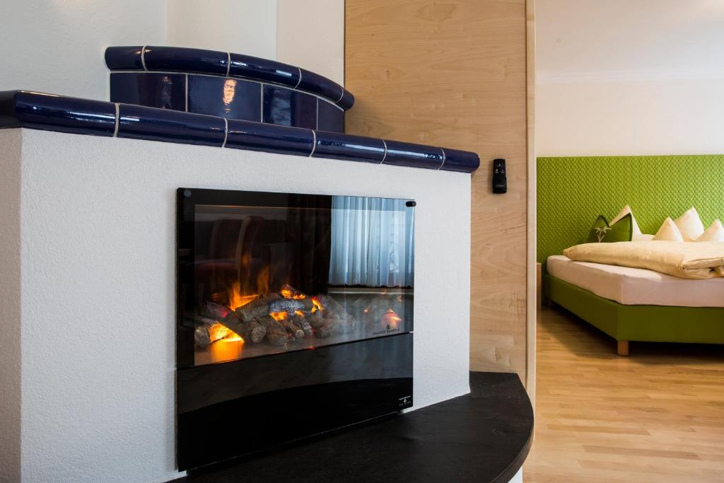 Moderns kamīns ar melnu stiklu un akmeņiem, kas rada siltumu un mājīgumu, redzams viesistabā ar zaļiem gultas piederumiem fonā.
