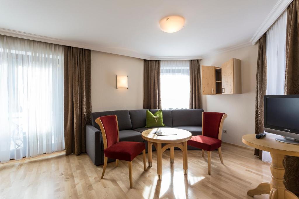 Mūsdienīgs viesistabas interjers ar pelēku dīvānu, sarkanu krēslu un koka galdu, apgaismots ar dabīgu gaismu no logiem.