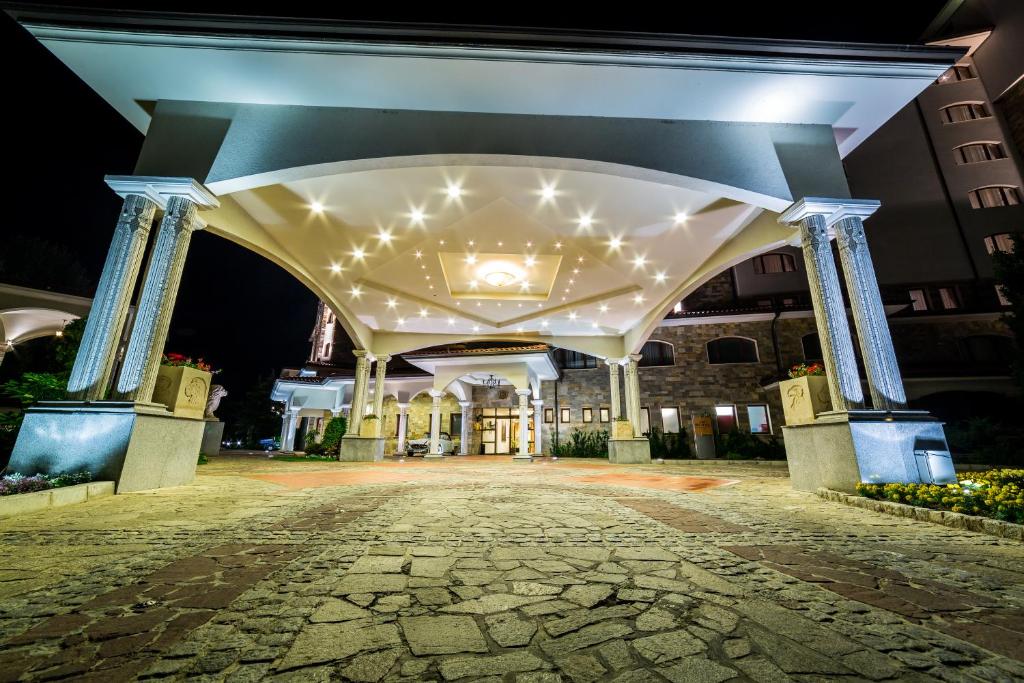 Eleganta viesnīcas ieeja ar apgaismojumu un akmens bruģi, kas rada viesmīlīgu atmosfēru. Naktī izgaismota, tā piesaista uzmanību un aicina apmeklētājus.