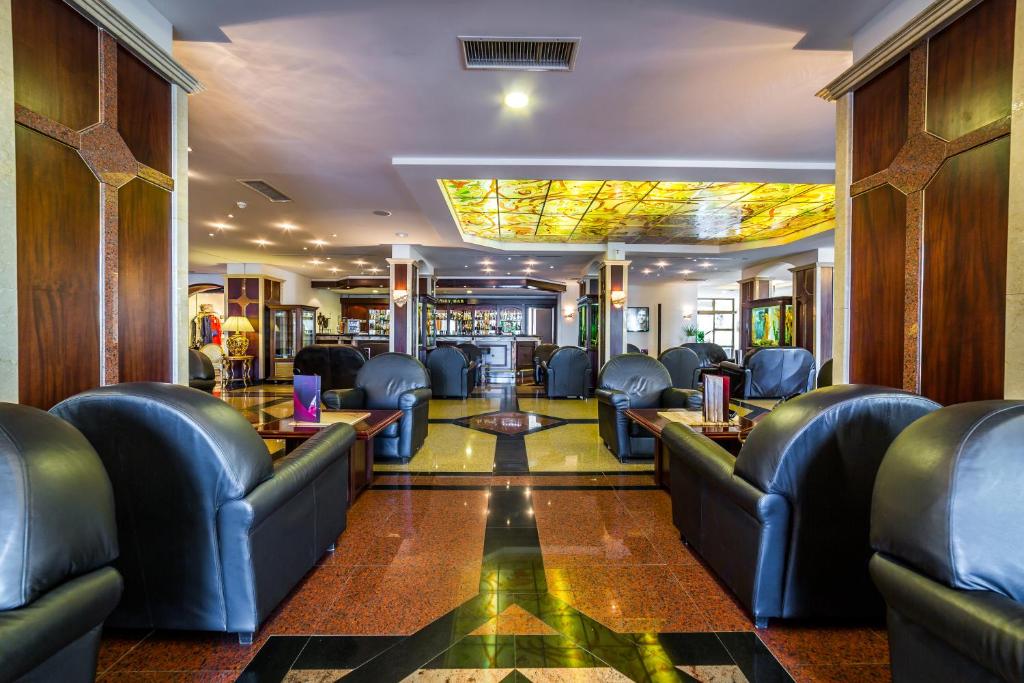 Moderns viesnīcas vestibils ar elegantiem ādas krēsliem un stilīgu apgaismojumu, kas radīts no krāsainām stikla paneļiem. Interjers apvieno mūsdienīgu dizainu ar klasiskām detaļām, radot aicinošu atmosfēru.