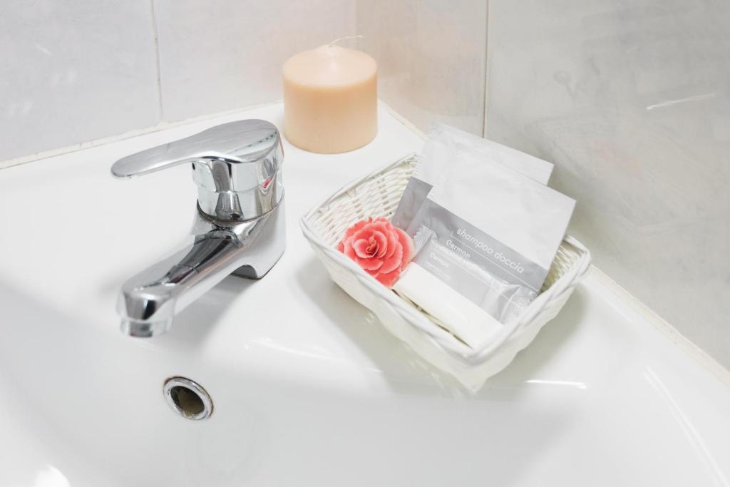 Vannas istabas skats ar spīdīgu krāna jaucēju, sveci un grozu, kurā ir šampūns un rozā zieds.
