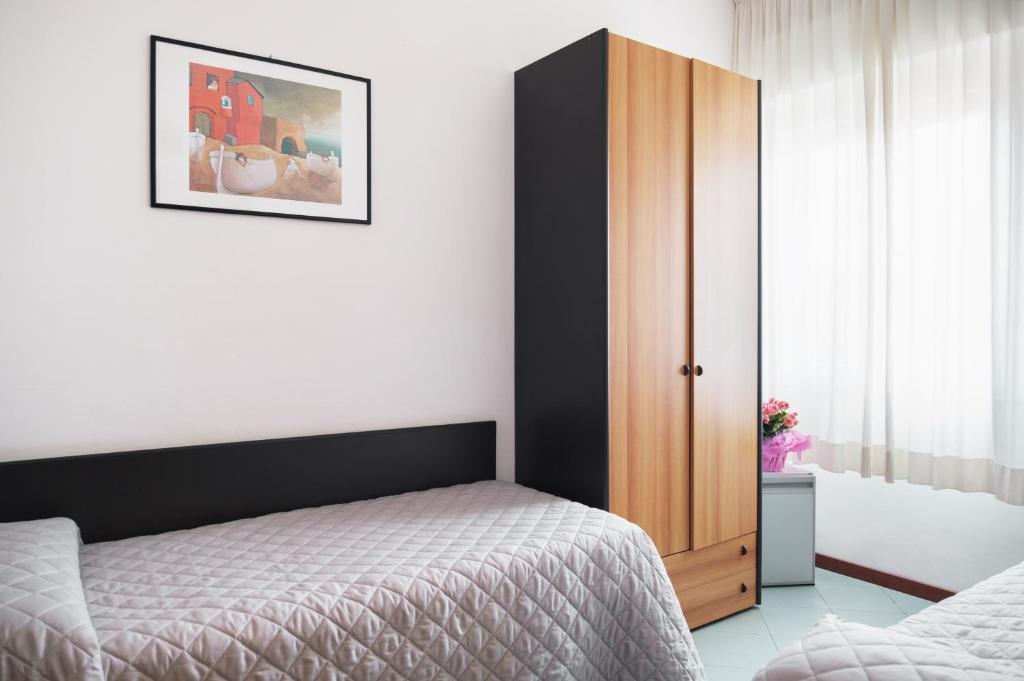 Gaiša guļamistaba ar divām gultām, koka skapī un mākslas darbu pie sienas. Logā ir plānas aizkaru, kas ļauj gaismai ienākt.