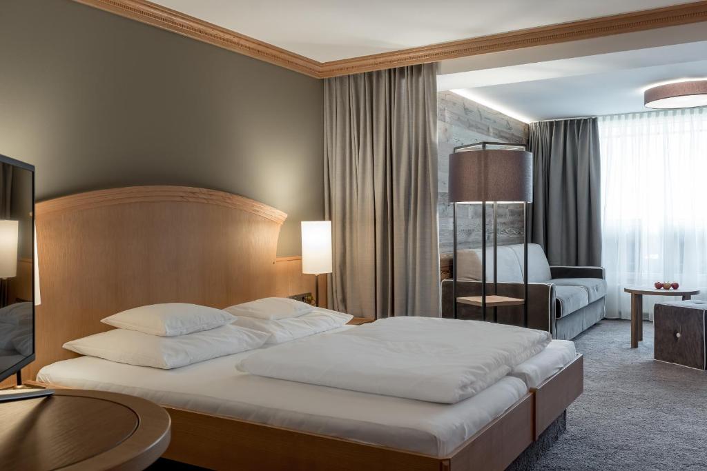 Mūsdienīgs viesnīcas numurs ar elegantu gultu, mīksto dīvānu un dabīgu apgaismojumu. Interjers ir veidots ar neitrālām krāsām un koka elementiem, radot mājīgu atmosfēru.