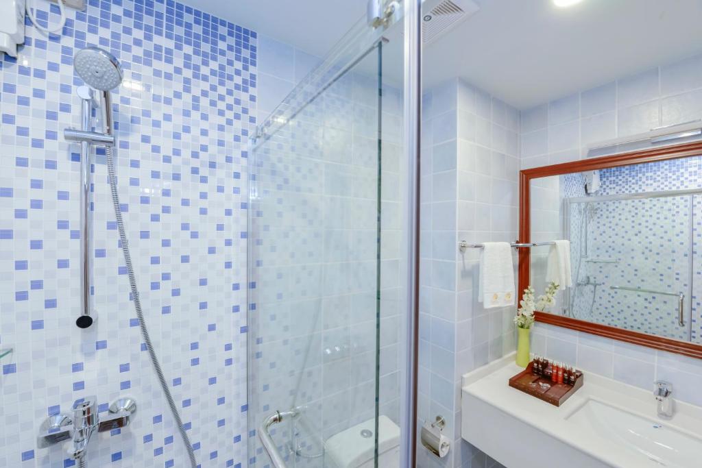 Mūsdienīgs vannas istabas interjers ar stikla dušas kabīni un mozaīkas flīzēm, kas piešķir telpai svaigu izskatu. Uz izlietnes atrodas kosmētikas komplekts un ziedi.