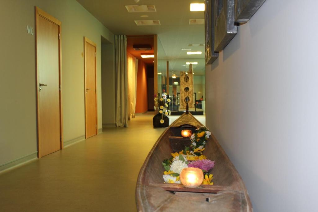 Korridorā redzama koka laiva, kas dekorēta ar ziediem un svecēm, radot relaksējošu atmosfēru. Fons ir ar vairākām durvīm un mīkstu apgaismojumu.
