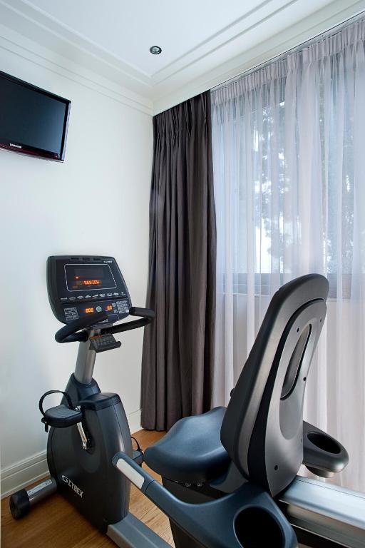 Mūsdienīgs sporta velosipēds, kas izvietots gaišā telpā ar lieliem logiem un aizkariem, kas ļauj ieplūst dabīgai gaismai. Uz sienas ir neliels televizors, kas piešķir papildus komfortu treniņu laikā.