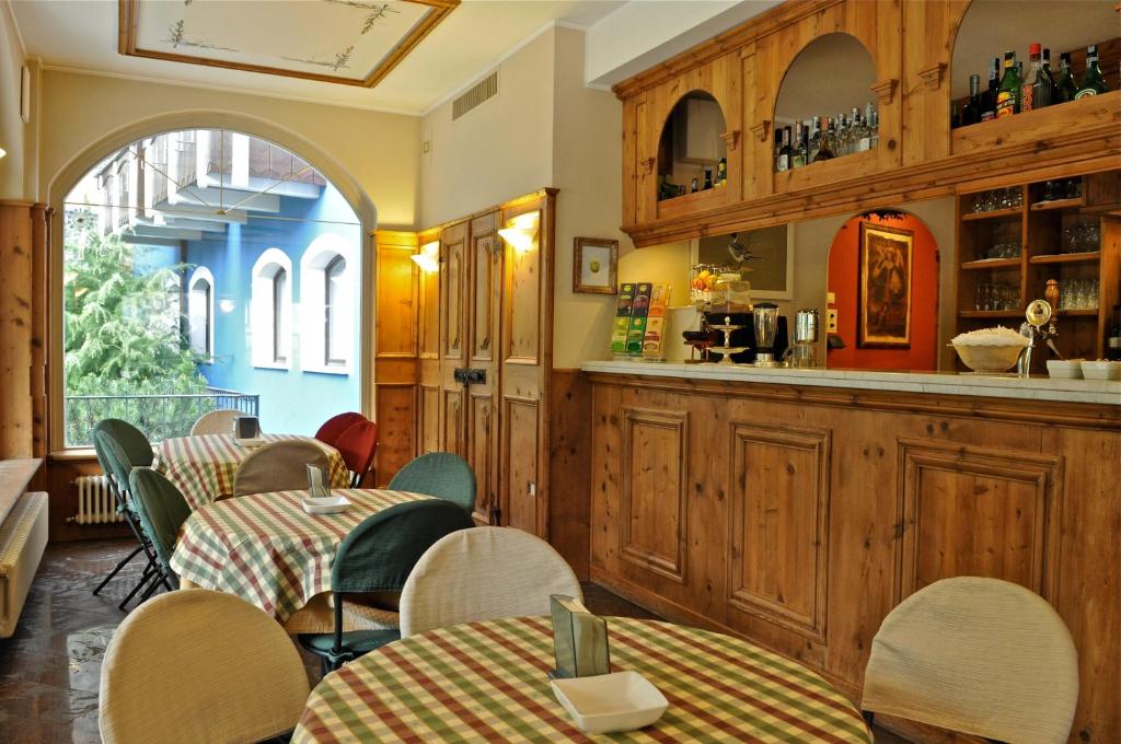 Grezns kafejnīcas interjers ar koka mēbelēm, galdiem ar svītrām un bāru, kas piedāvā dzērienus. Logi dod skatu uz zaļo dārzu un blakus esošo ēku.