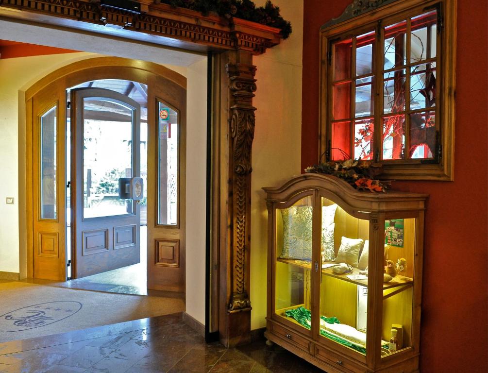 Klasiska interjera skats ar koka durvīm un vitrīnu, kurā redzami dažādi priekšmeti. Gaisma ieplūst caur durvīm, radot siltu atmosfēru.