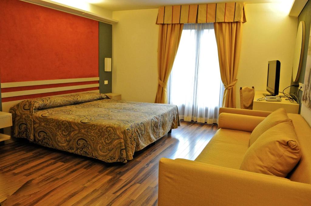 Mūsdienīgs viesnīcas numurs ar divguļamo gultu, dīvānu un televizoru. Logi ar dzeltenām aizkariem nodrošina dabisko apgaismojumu.