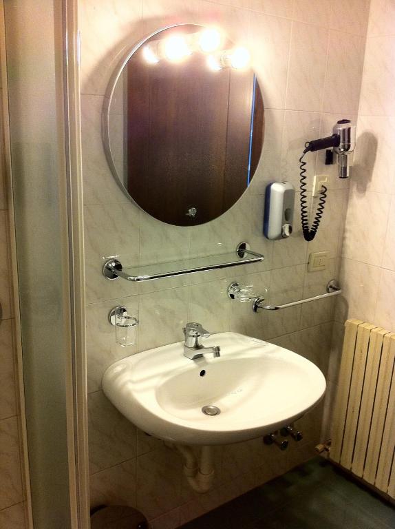 Vannas istabas interjers ar apaļu spoguli, higiēnas piederumiem un izlietni, kas nodrošina ērtu un funkcionālu vidi. Apgaismojums virs spoguļa piešķir telpai siltu atmosfēru.