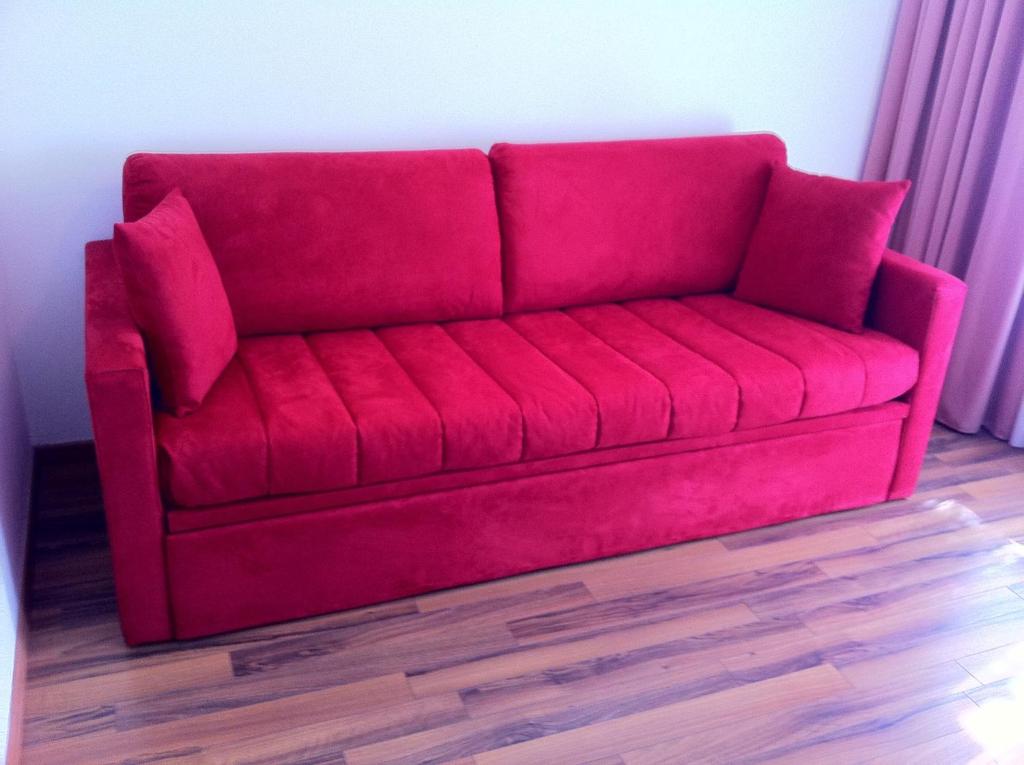 Sarkans dīvāns ar divām spilvenēm, kas piešķir telpai modernu un dzīvīgu izskatu. Dīvāns ir ērts un piemērots gan atpūtai, gan viesu uzņemšanai.