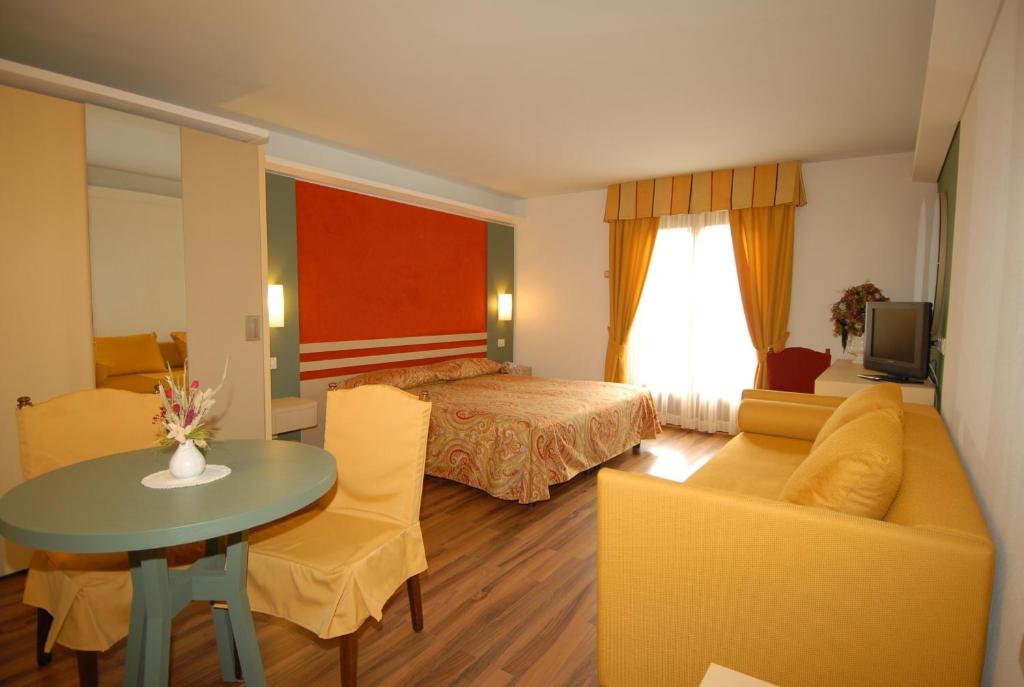 Mūsdienīga viesnīcas numura interjers ar ērtu gultu, dīvānu un galdu, kas apgaismots ar dabiskiem gaismas avotiem. Siltas krāsas un viesmīlīga atmosfēra rada patīkamu atpūtas vidi.