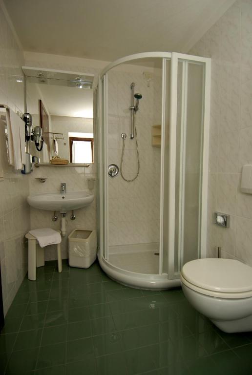 Mūsdienīgs vannas istabas interjers ar dušu, izlietni un tualeti, kurā dominē gaišas krāsas un gluda flīzēta grīda.