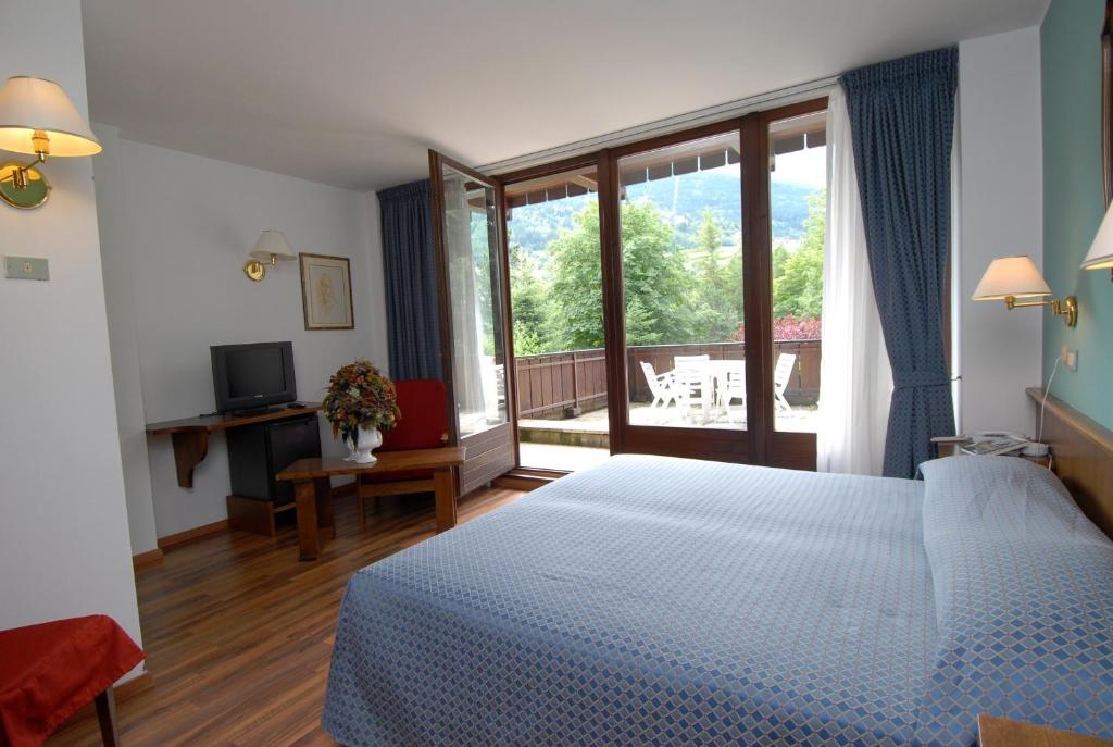 Gaiša viesnīcas numura iekārtojums ar plašu logu, caur kuru redzams dārzs. Numurā ir gulta, rakstāmgalds, televizors un sēdvieta.