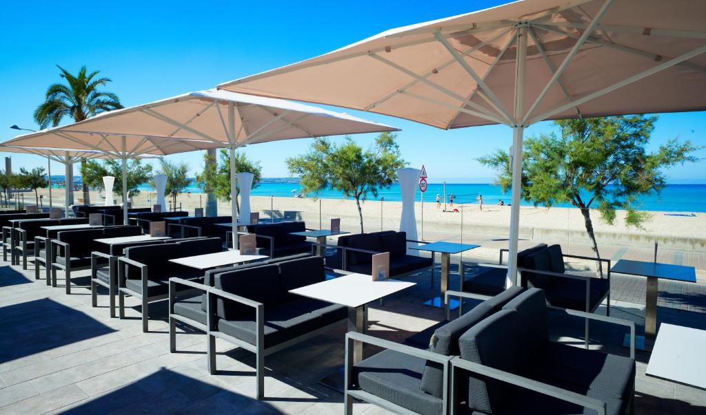 Mūsdienīgs pludmales kafejnīcas terase ar ērtām mēbelēm un saulessargiem, skatoties uz smiltīm un jūru. Ideāla vieta relaksācijai un atpūtai saulainā dienā.