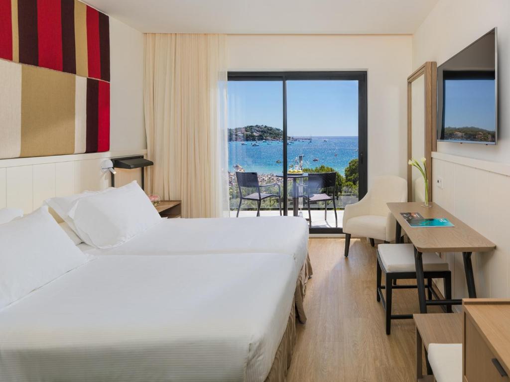 Mūsdienīga viesnīcas istaba ar divām gultām un skatu uz jūru. Istabā ir televizors, rakstāmgalds un balkons, nodrošinot komfortablu atpūtu.