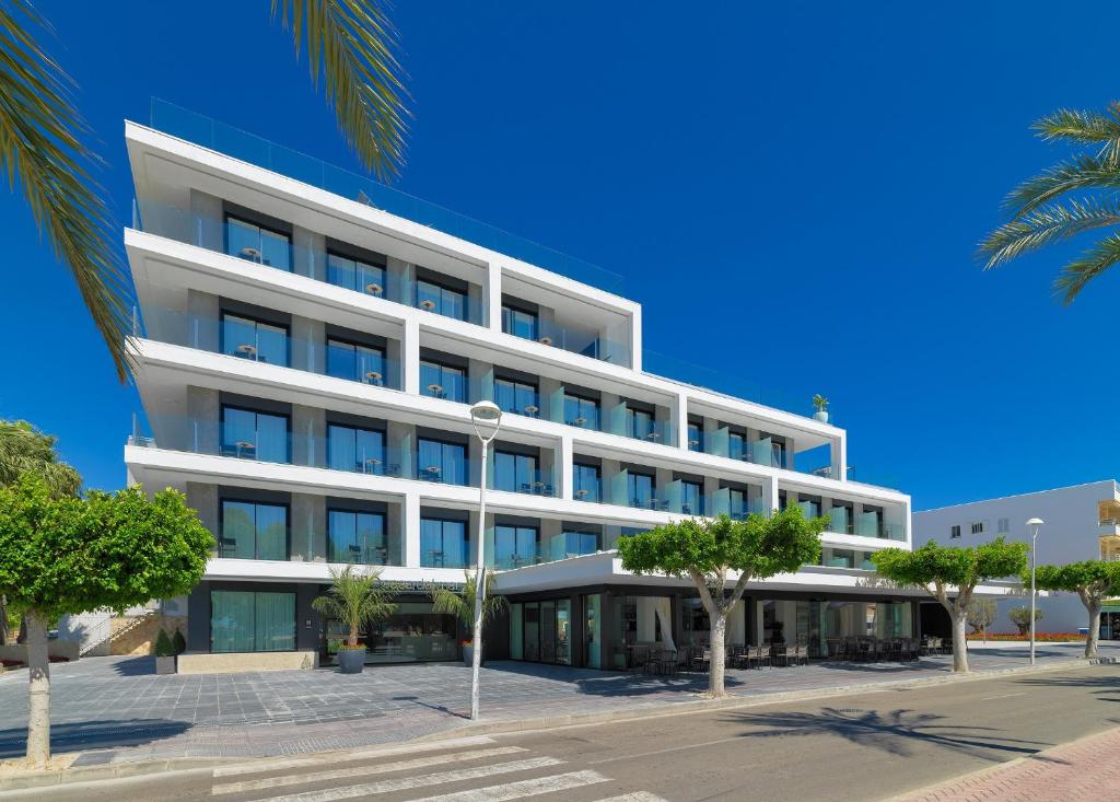 Mūsdienīga viesnīca ar plašiem logiem un balkoniem, kas atrodas saulainā dienā. Apkārt viesnīcai ir zaļi koki un gājēju celiņš.