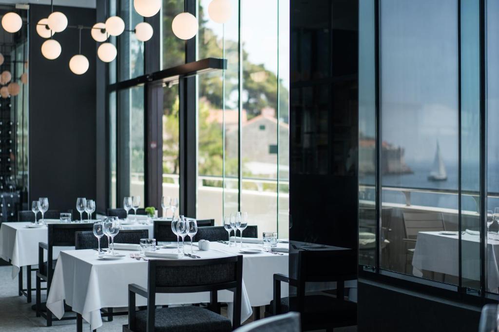 Mūsdienīgs restorāna interjers ar baltām galdautām klātiem galdiem, izsmalcinātiem galda piederumiem un stikla sienām, kas paver skatu uz jūru. Gaismas ķermeņi piešķir siltumu un eleganci.