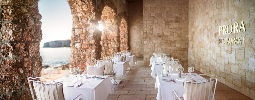 Elegants restorāns ar baltām galdiem, kas izvietoti zem arku konstrukcijām, piedāvā skatu uz jūru. Prora restorāna nosaukums ir izcelts uz akmens sienas.