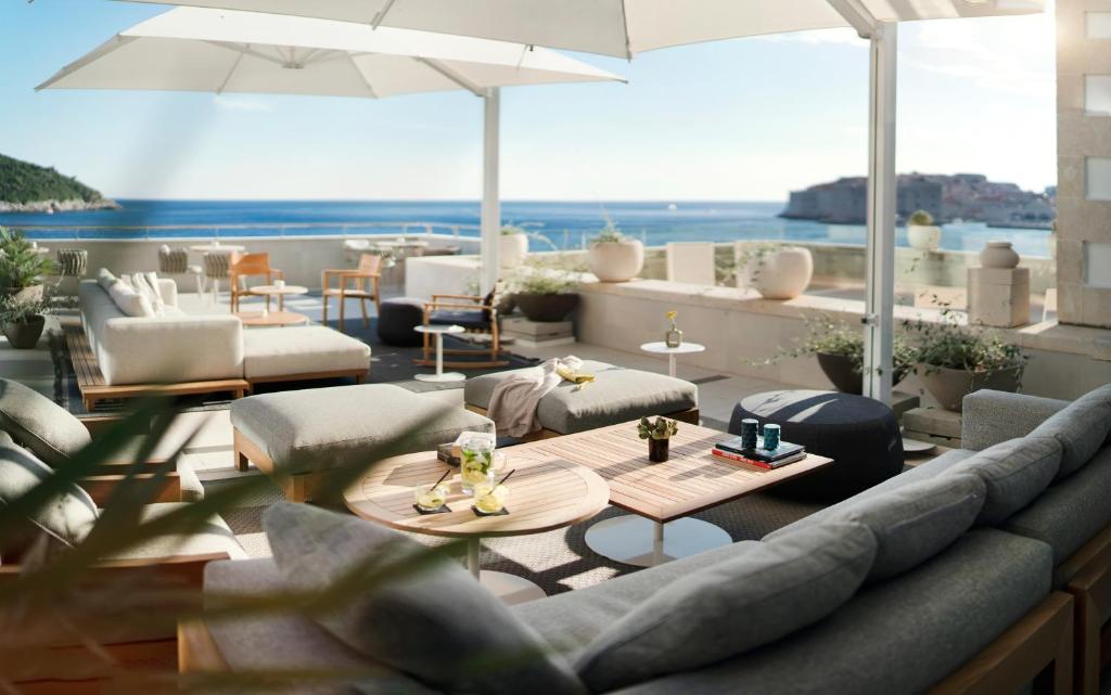 Elegantā terase ar mīkstiem dīvāniem un skatu uz jūru, kurā atrodas galdi un augi, ideāli piemērota relaksācijai un atpūtai.